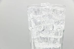 Close-up of a glass filled with sparkling water and ice cubes, ideal for refreshing summer drinks.