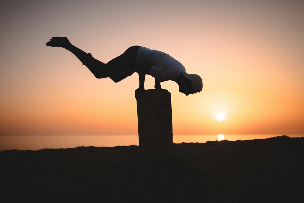 a person doing a handstand on a pole at sunset