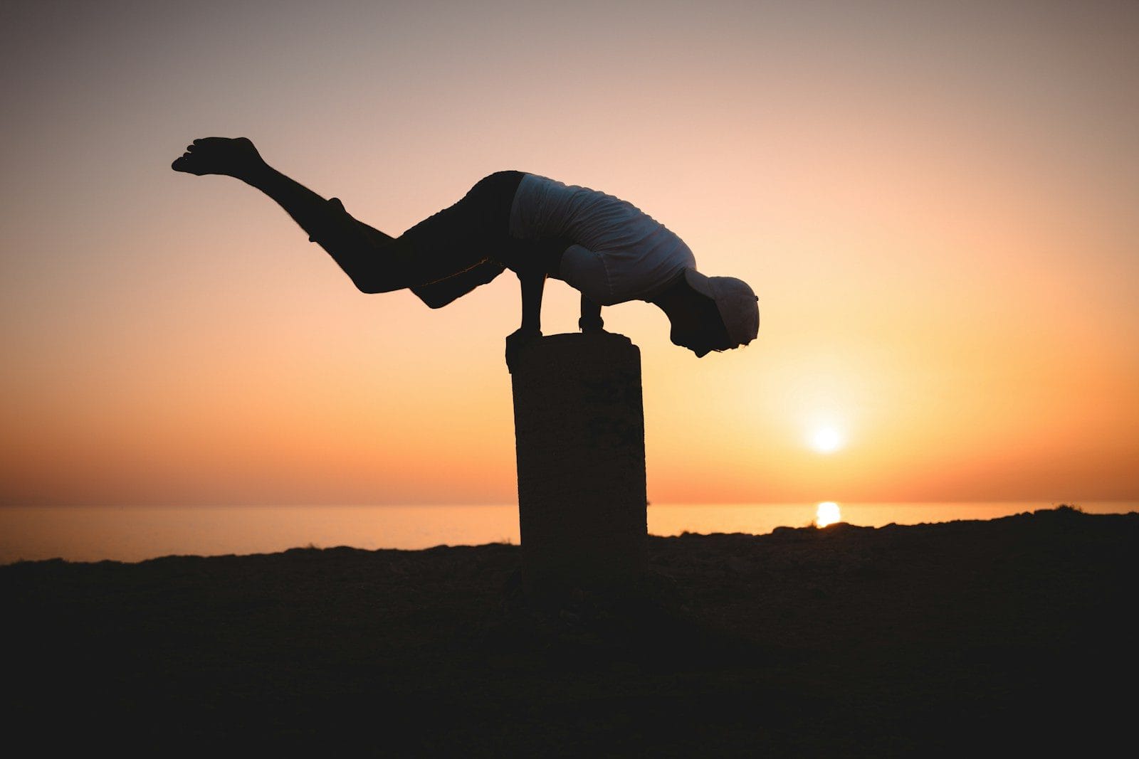 a person doing a handstand on a pole at sunset